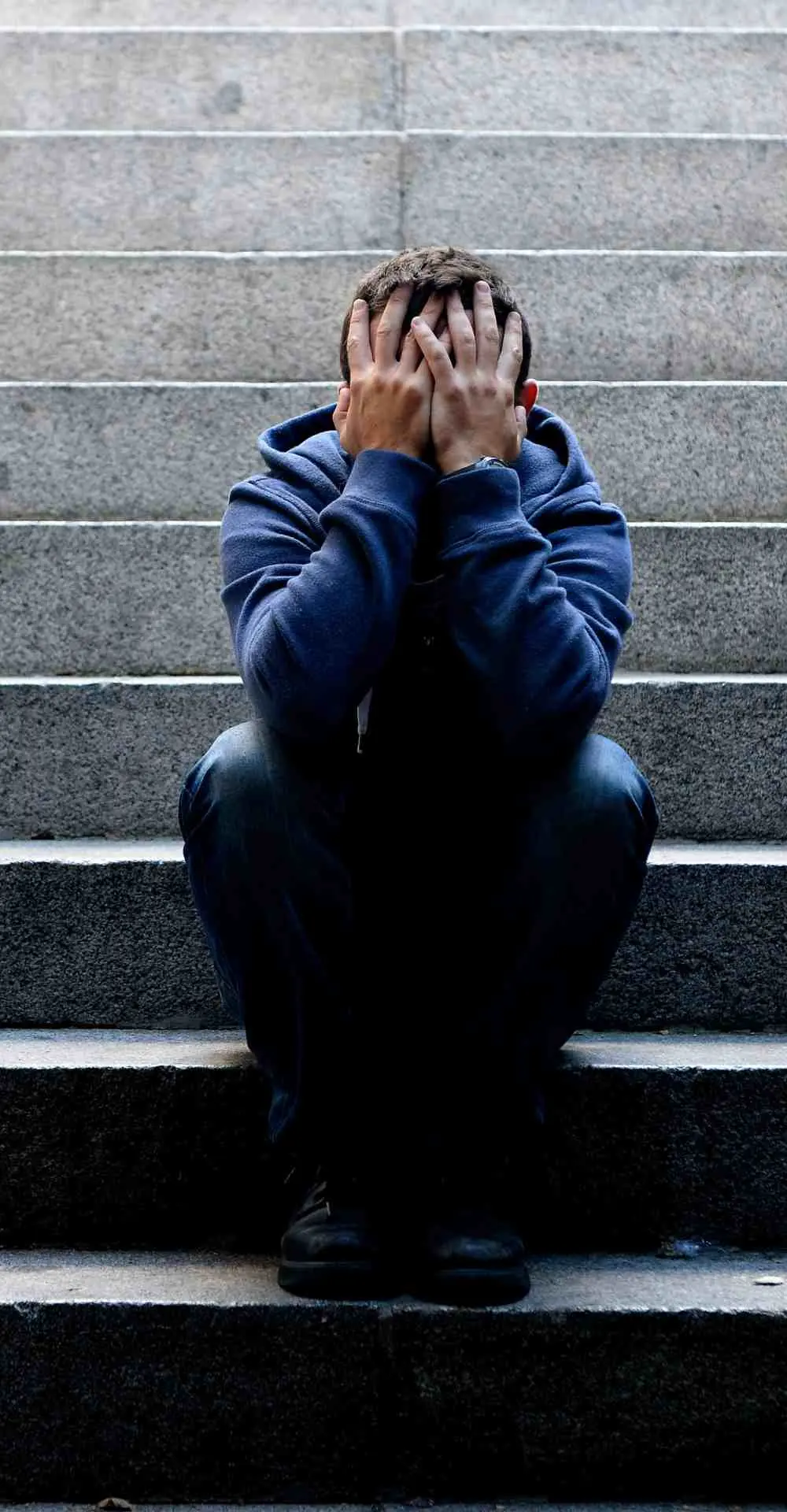 Man sitting on outdoor stairs with head in hands representing depression symptoms