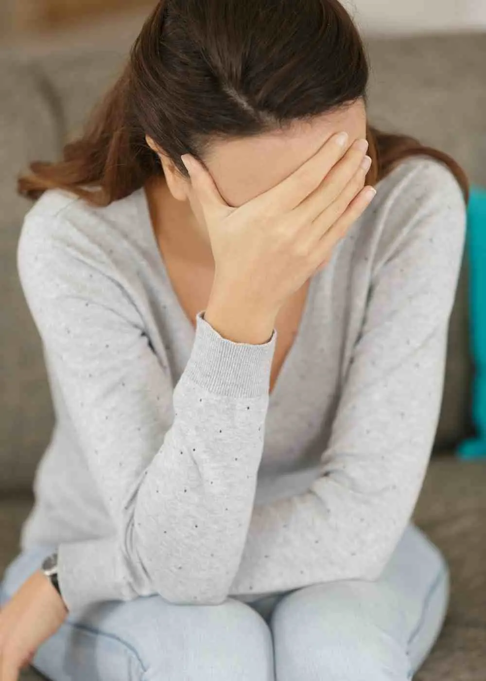 Woman sitting on a couch covering her face showing emotional distress and anxiety