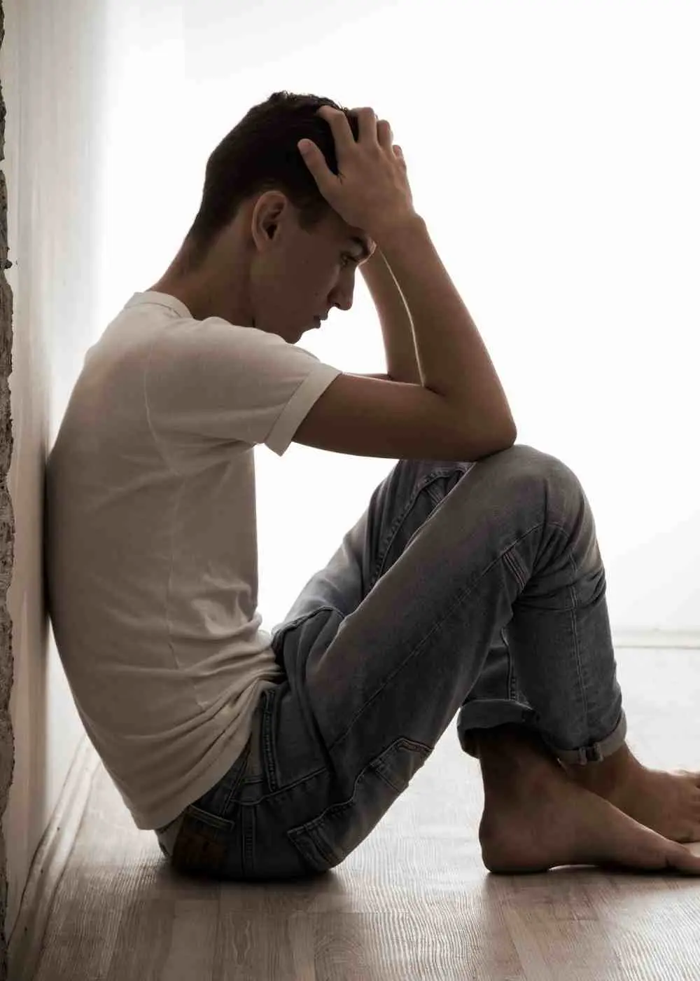 Young man sitting on the floor alone holding his head showing isolation and depression