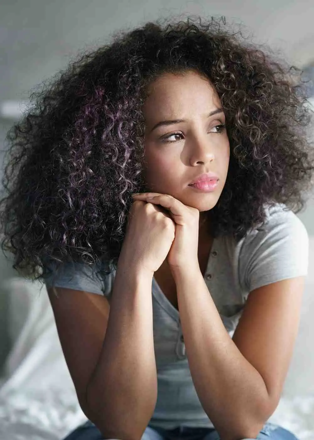 Young woman sitting on a bed in quiet reflection, showing emotional distress and possible signs of needing professional mental health treatment
