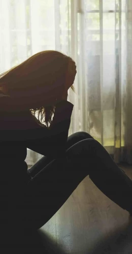 Woman sitting on the bedroom floor with her head in her hand, illustrating depression symptoms